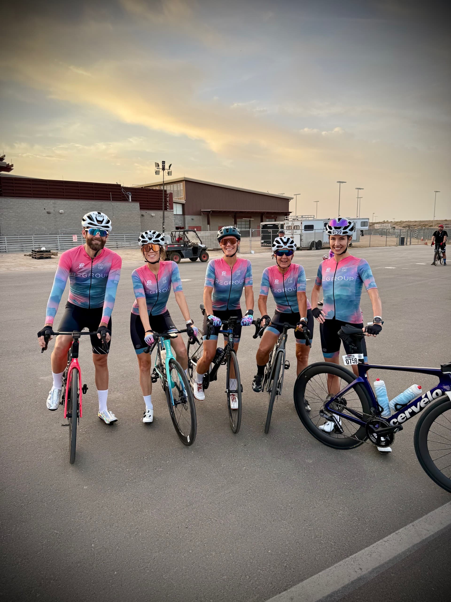 Five riders wearing matching pink and blue Regroup kits at sunset